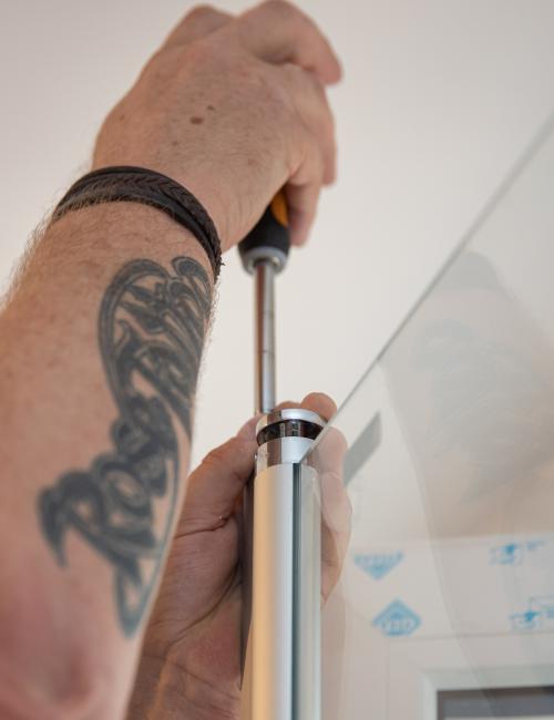 Bildausschnitt mit zwei Händen eines Handwerkers bei der Montage einer Glas-Duschwand.