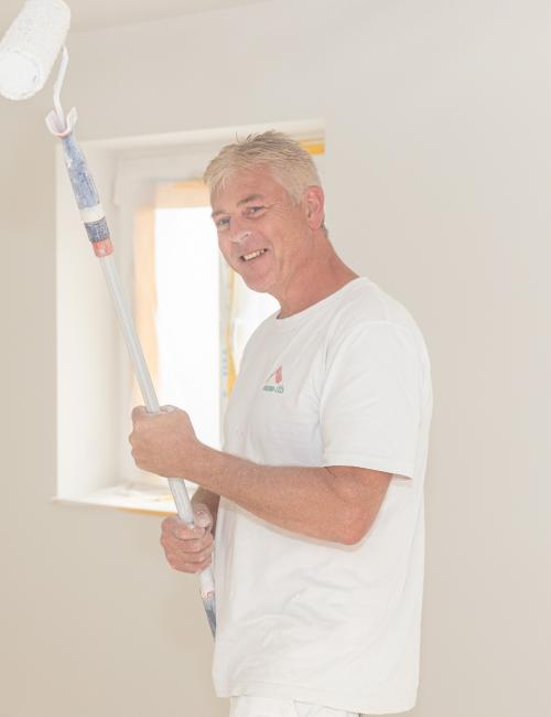 lächelnder Malermeister mit weißer Farbrolle beim Malern eines Zimmers
